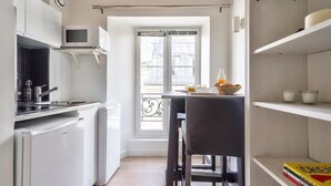 Une cuisine compacte avec des appareils électroménagers blancs, un coin repas avec une table et des chaises, et une vue par la fenêtre.