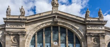 Un imposant bâtiment à l’architecture classique, doté d’une grande fenêtre en arc de cercle et de statues sur la façade.
