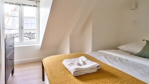 Une chambre à coucher avec un lit, une fenêtre, une commode et une vue sur les bâtiments à l’extérieur.