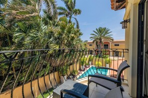 Un balcón con vistas a una piscina, rodeado de exuberante vegetación y palmeras.