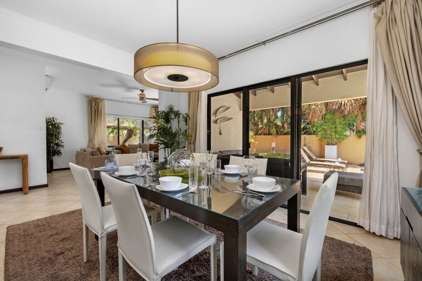 A dining area with a glass table, white chairs, and a modern pendant light.