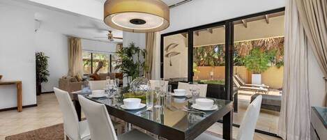 A dining area with a glass table, white chairs, and a modern pendant light.