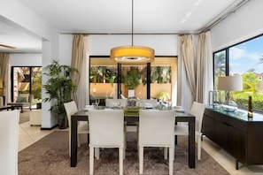 Un comedor moderno con una mesa de vidrio, sillas blancas y una lámpara colgante central.