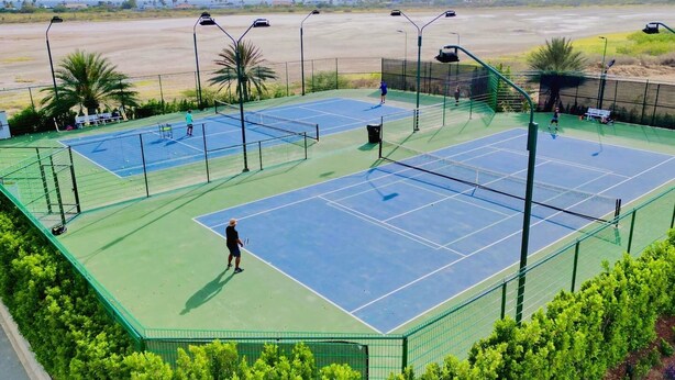 A tennis court with multiple courts, surrounded by a green fence, and palm trees in the background. - Exquisite Poolside Living in Diamante 165 by Bocobay (Noord)