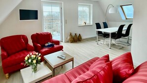 A modern living room with red sofas, a dining area with black chairs, and large windows.