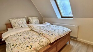 A bedroom with a sloped ceiling, a wooden bed, a radiator, and a window with a view of trees.