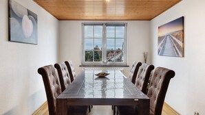Comedor con mesa y sillas de madera, vistas por una ventana grande y obras de arte en las paredes.