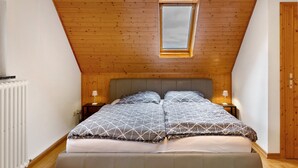 Un dormitorio con techo inclinado, tragaluz, cama con ropa de cama estampada, lámparas de noche y una puerta de madera.