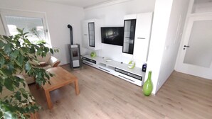 A modern kitchen with a TV, white cabinets, a wooden table, and a green vase. - Holiday Home 'Ferienhaus Kesper' with Mountain View, Private Terrace & Wi-Fi (Schottwien)