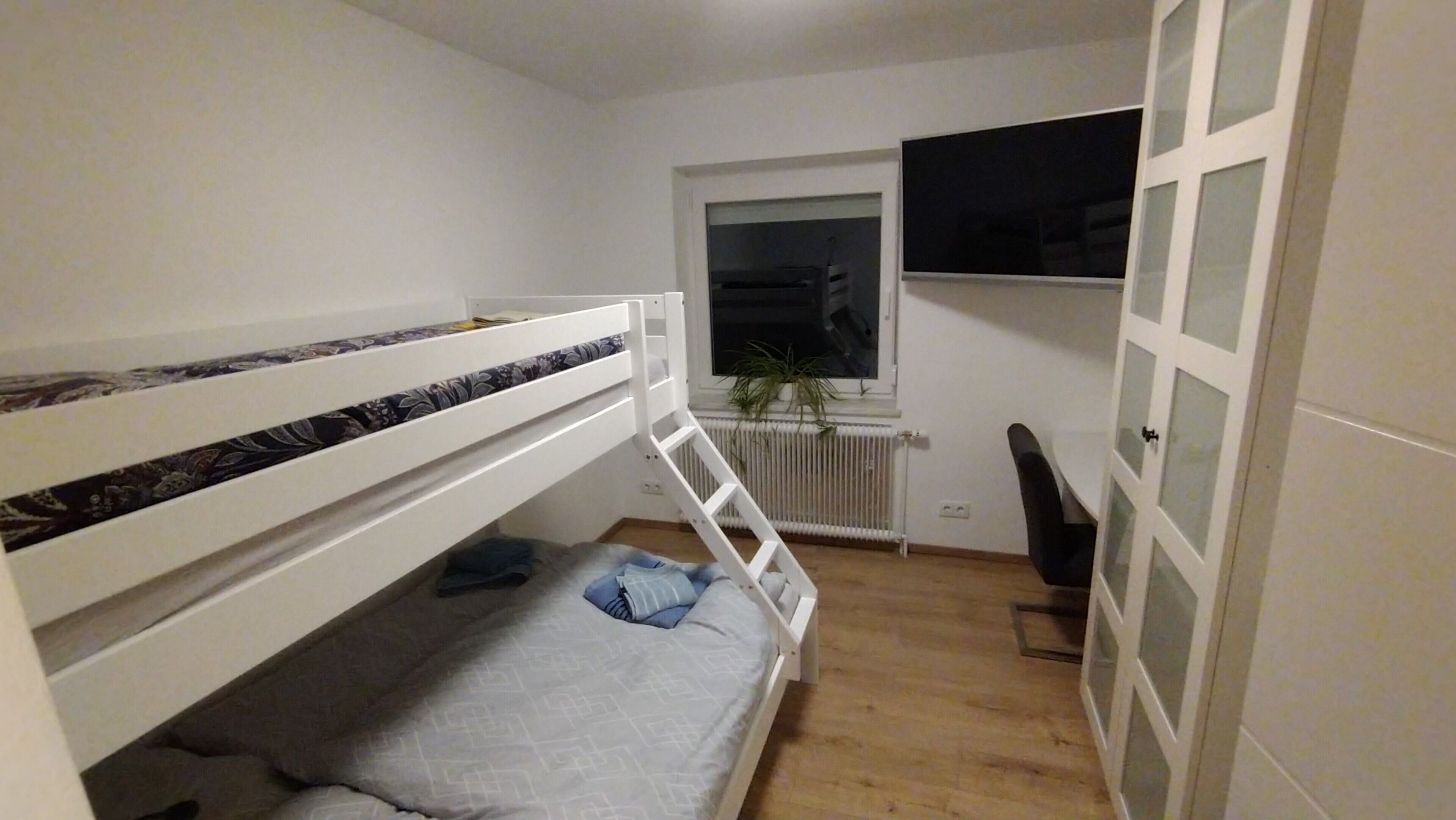 Une chambre avec un lit superposé, un radiateur, une fenêtre et une porte.