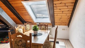 Comedor con mesa de madera, sillas, planta en maceta y tragaluz.