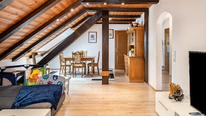 Una habitación estilo loft con techo inclinado, vigas de madera, un comedor con mesa y sillas, un televisor y un pequeño excavador de juguete.