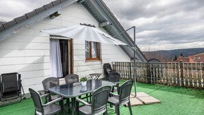 Una casa blanca con techo inclinado, una mesa de comedor con sillas, una planta en maceta y vistas a las montañas.