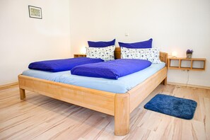 Un lit double avec une literie bleue, une tête de lit en bois, une table de chevet avec une lampe et une petite étagère avec une plante.