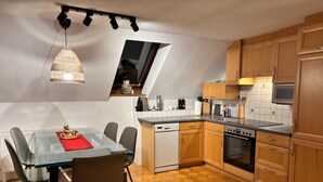 Une cuisine moderne avec des meubles en bois, un lave-vaisselle, un four et un coin repas comprenant une table et des chaises en verre.