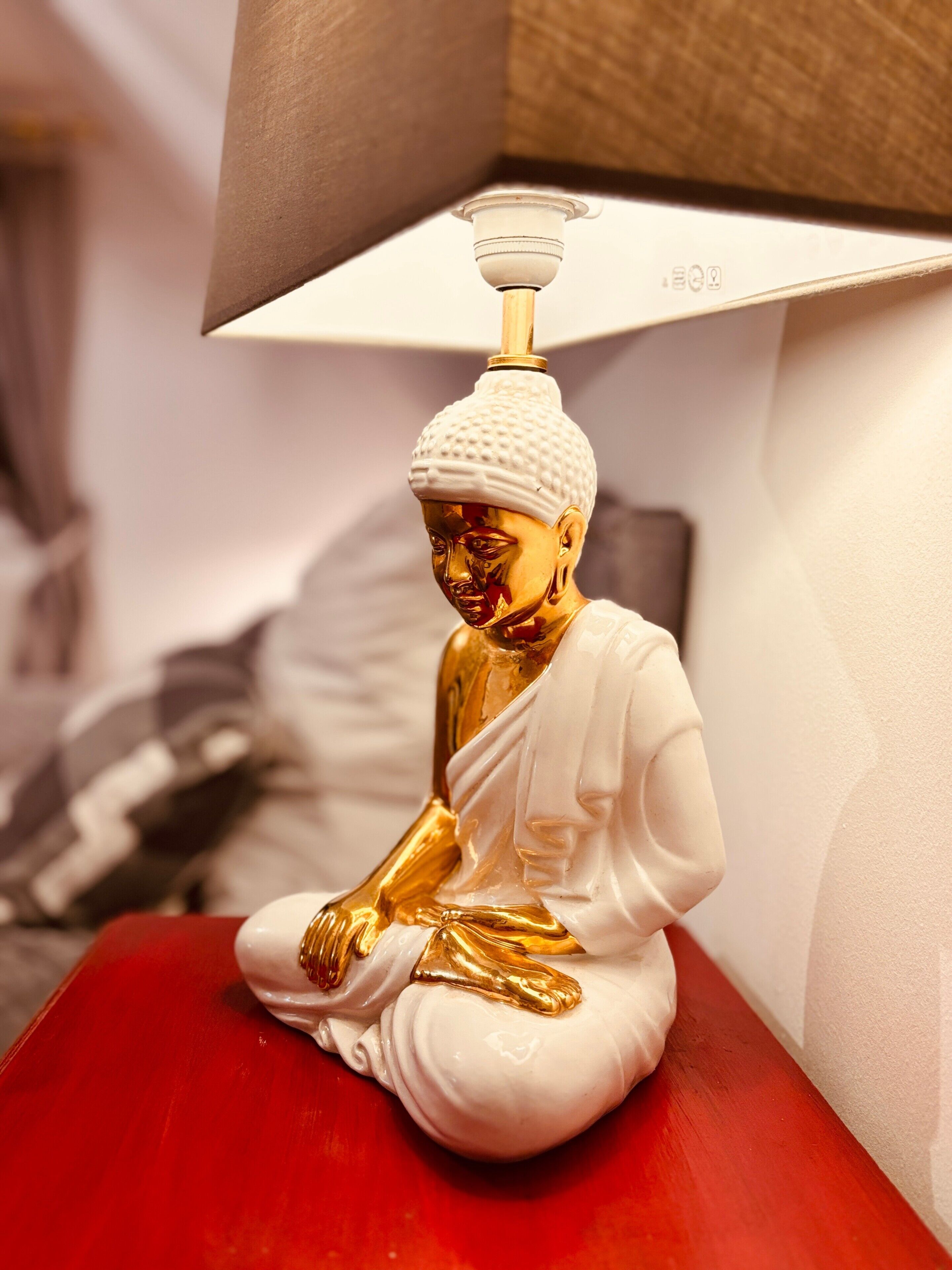 Een gouden Boeddhabeeld op een rode ondergrond, verlicht door een witte lamp.