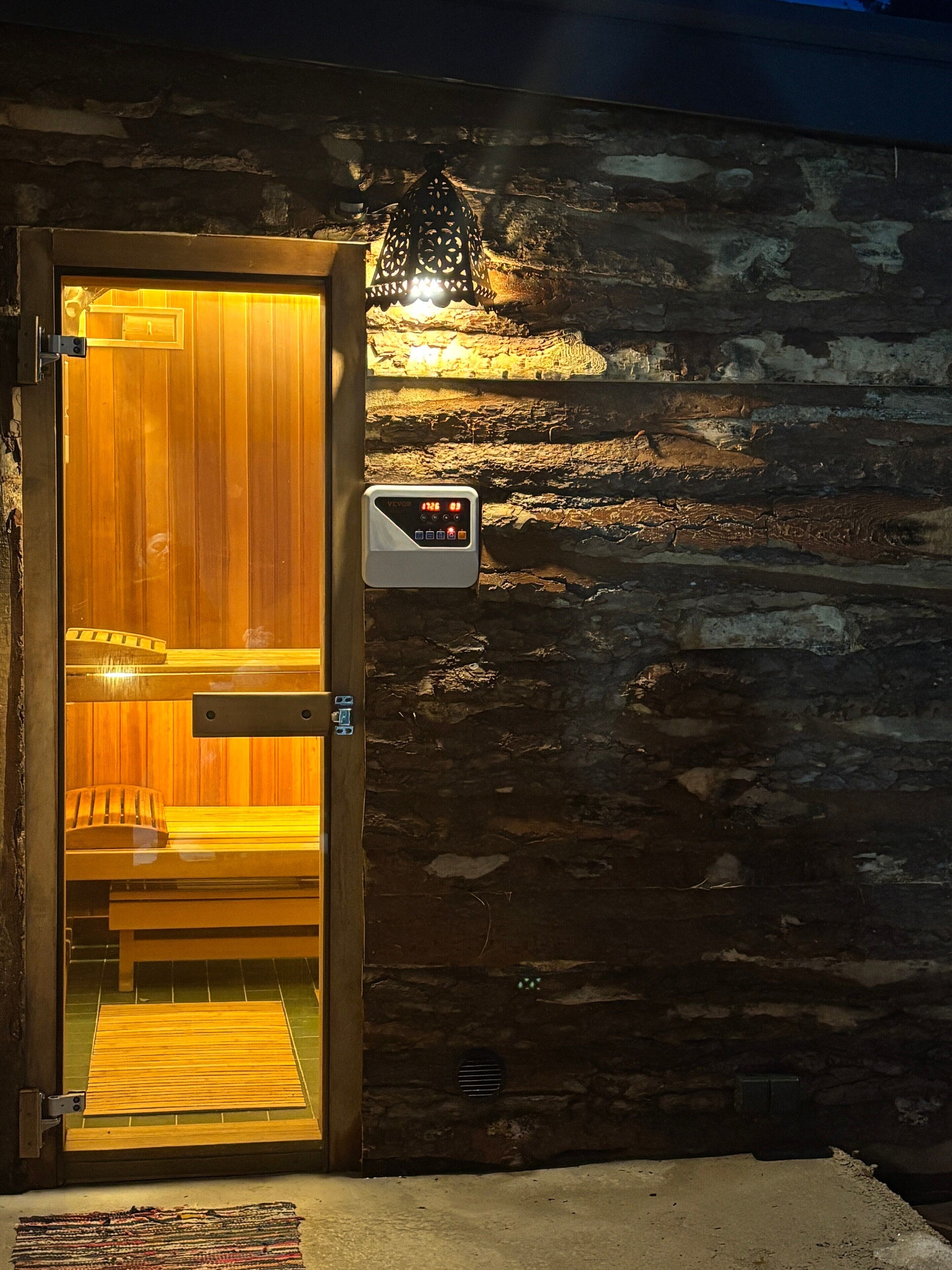 Une porte en bois dotée d’un écran numérique, une salle de sauna avec des bancs et un mur en pierre.