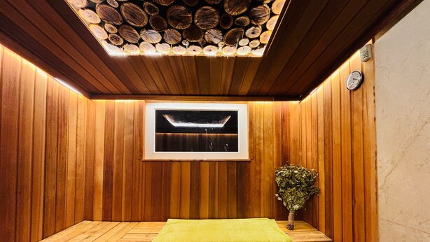 Un sauna aux murs en bois, avec un banc, une petite table sur laquelle est posée une serviette verte, et une horloge au mur.