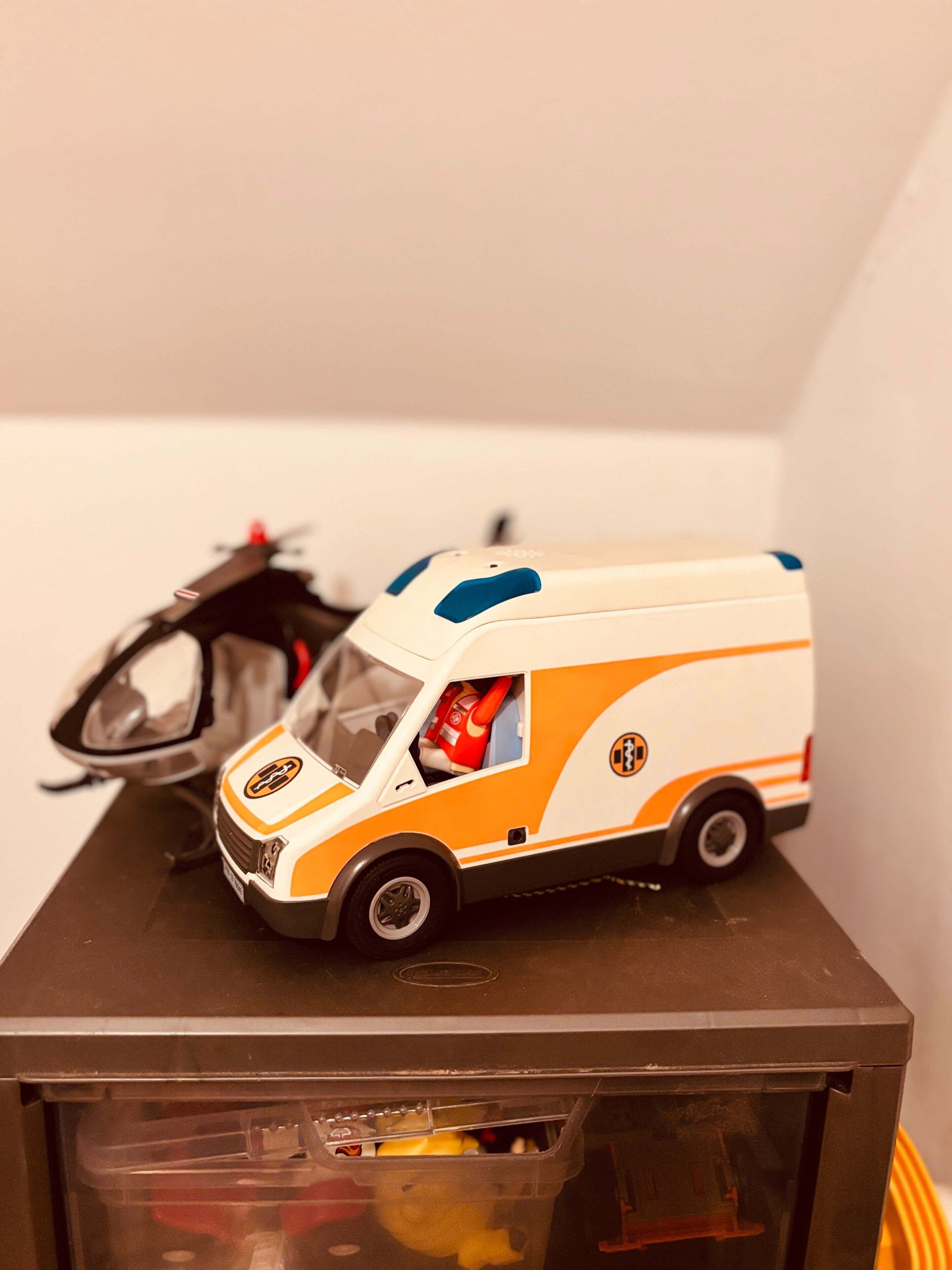 Ein Spielzeug-Krankenwagen im Seitenblick, ein Spielzeug-Hubschrauber und ein Spielzeug-Krankenwagenfahrer.