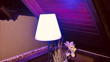 A room with a wooden ceiling, a hanging lantern, a table lamp, and a vase with dried plants.