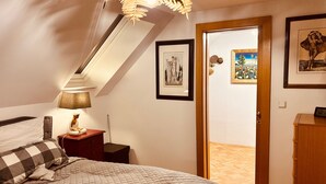 Une chambre à coucher comprenant un lit, une table de chevet, une lampe et une porte donnant sur une autre pièce.
