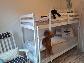 Ein Etagenbett mit einem Stofftier am unteren Bett, einem gestreiften Kissen und einem kleinen Stuhl mit Sitzkissen.
