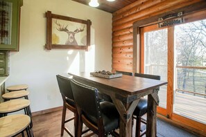 A wooden dining table with four chairs, a framed deer head artwork, and a window with a view of trees. - Hilltop Haven • Pool, Hot Tub & Game Loft (Fayetteville)