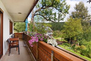 Un balcon avec une table et des chaises, une balustrade en bois et une vue sur une maison et la verdure.
