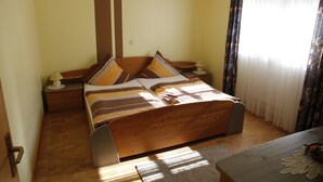 A bedroom with a wooden bed, two bedside tables, a nightstand, a window with curtains, and a wooden floor. - Apartment 'Stark bis 4 Personen' with Wi-Fi (Scheßlitz)