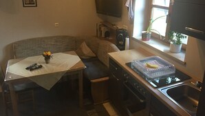 A compact kitchen with a dining area, a television, a window with plants, and a small table with a vase. - Apartment 'Stark bis 4 Personen' with Wi-Fi (Scheßlitz)