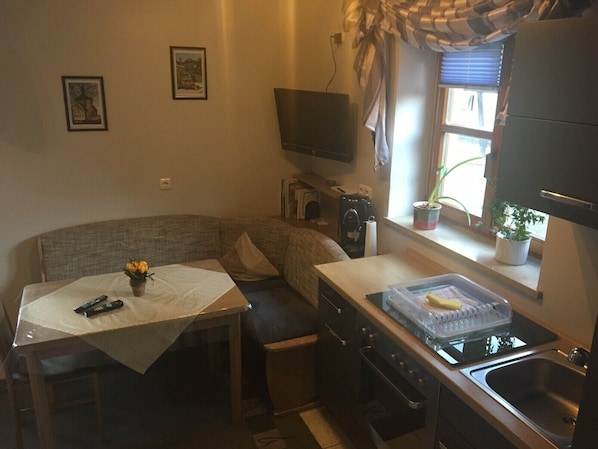 Una cocina compacta con comedor, televisión, ventana con plantas y una pequeña mesa con un florero.