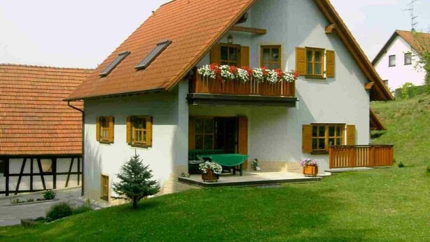 A two-story house with a sloped roof, wooden shutters, and a balcony with flowers. - Apartment 'Stark bis 4 Personen' with Wi-Fi (Scheßlitz)