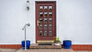 A red door with a glass panel, a metal door handle, and a small porch with two blue planters. - Holiday Home 'Haus Lahrsen' with Private Terrace, Shared Garden and Wi-Fi (Wesselburen)