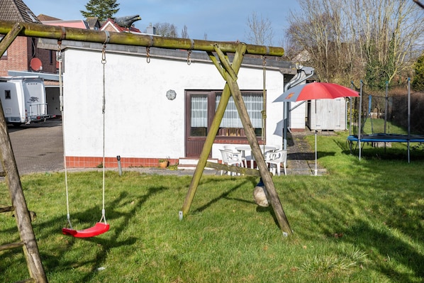 Une balançoire, un bâtiment blanc et un parasol rouge.