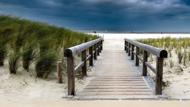 A wooden boardwalk leading to a beach with dunes and a cloudy sky. - Holiday Home 'Haus Lahrsen' with Private Terrace, Shared Garden and Wi-Fi (Wesselburen)
