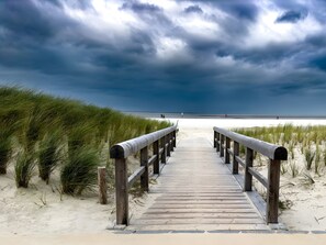 Une promenade en bois menant à une plage bordée de dunes, sous un ciel nuageux.
