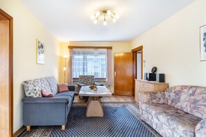 A living room with a sofa, a chair, a table, a patterned rug, and a ceiling light fixture.