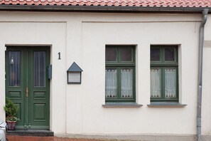 A building with a green door, two windows with lace curtains, and a number '1' on the wall.