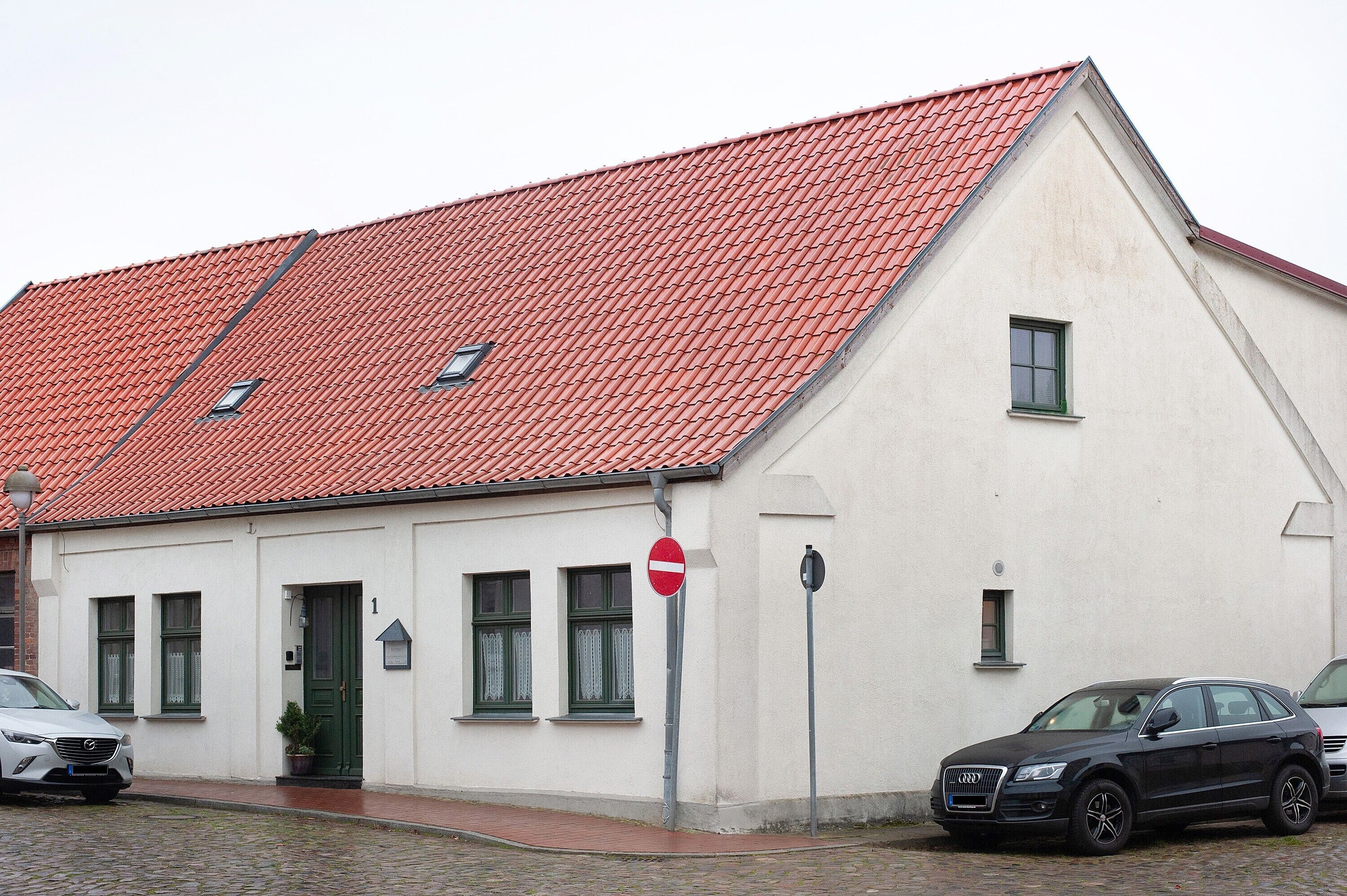 Un bâtiment avec un toit recouvert de tuiles rouges, une façade blanche et une voiture noire garée devant.