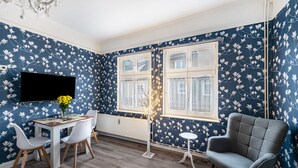 A room with a dining table, chairs, a TV, a window with white frames, and a patterned wall. - Apartment 'Studio Zur »Alten Schmiede«' with Wi-Fi (Laage)