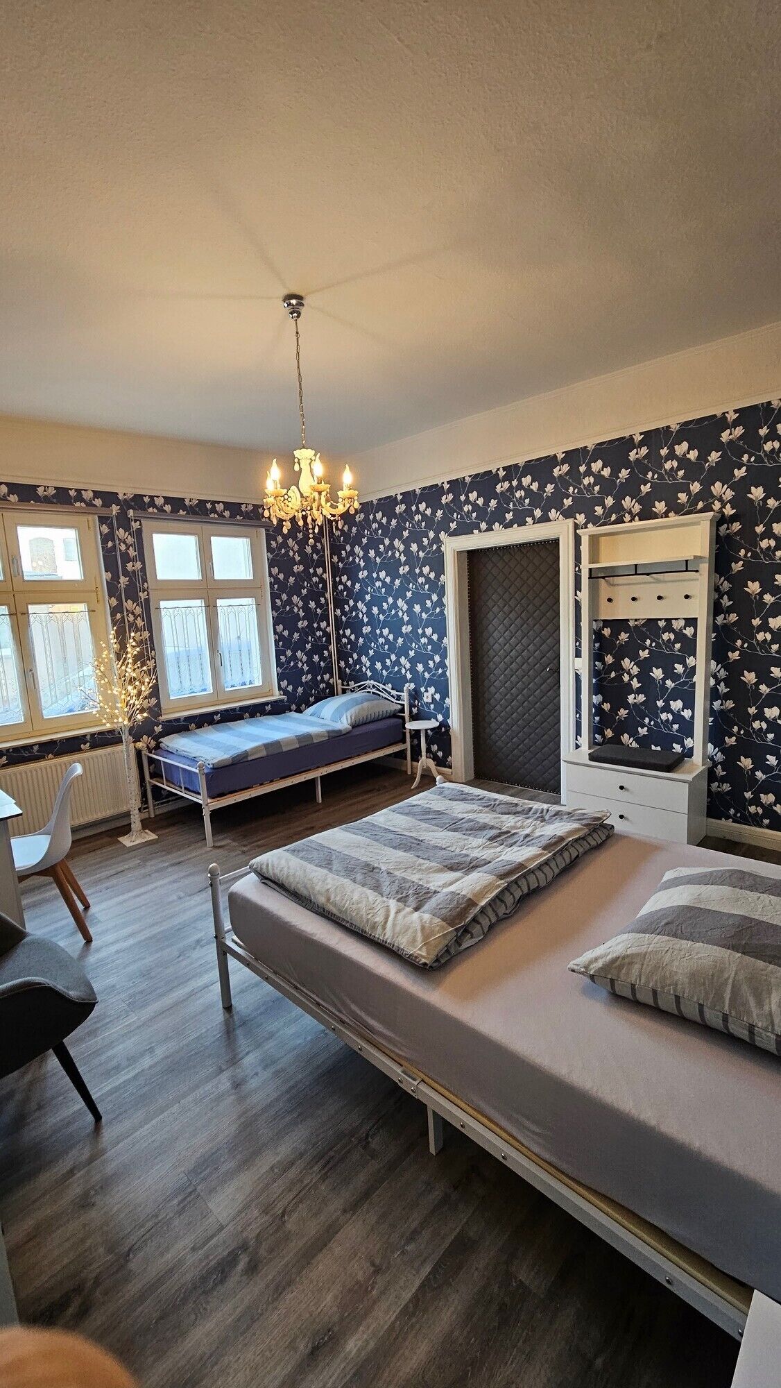 Ein Schlafzimmer mit einem Etagenbett, einem Schreibtisch, einem Stuhl, einer Chandelier und einem Fenster.