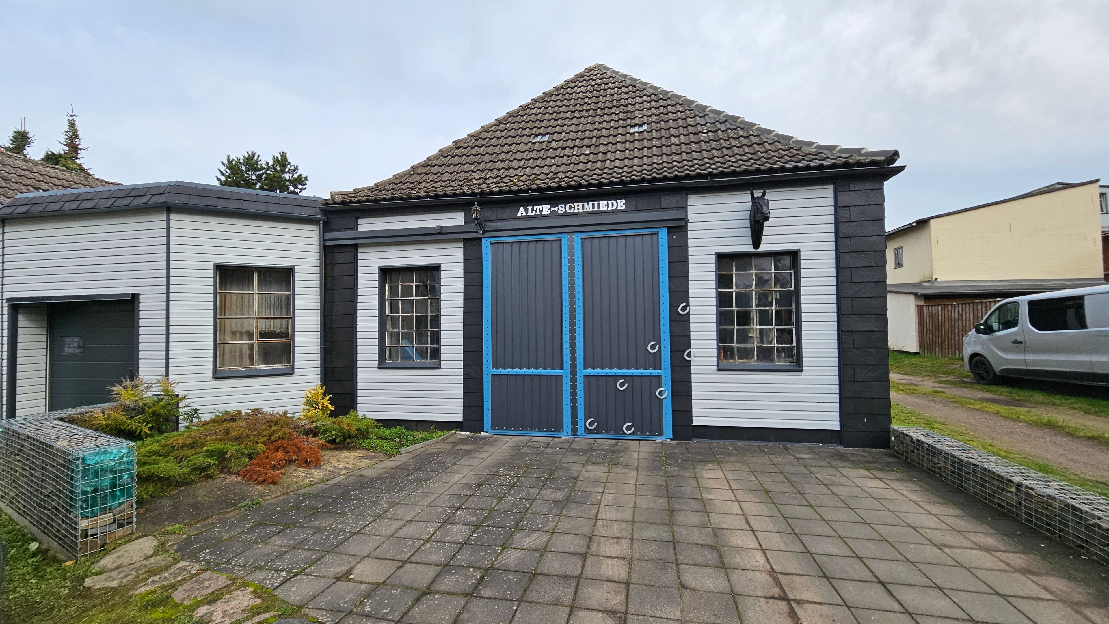 A building with a blue door, a tiled roof, and a paved entrance.