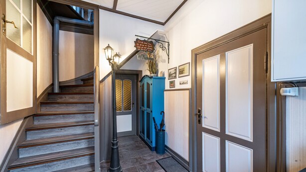 A hallway with a wooden staircase, a blue cabinet, and a door with a doormat. - Apartment 'Studio Zur »Alten Schmiede«' with Wi-Fi (Laage)