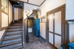 A hallway with a wooden staircase, a blue cabinet, and a door with a doormat.