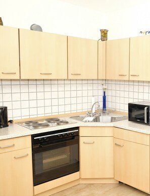 A compact kitchen with a stove, oven, microwave, sink, and light-colored cabinets.