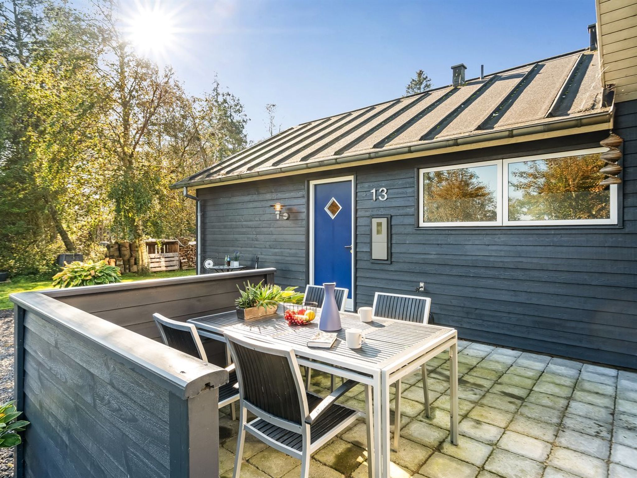 A house with a blue door, number 13, and a patio with a table and chairs.