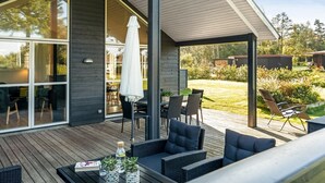 Eine moderne Außenterrasse mit Korbmöbeln, einem Tisch mit einem Buch und Flaschen sowie einer großen Glasdoor, die zu einer Patio führt.