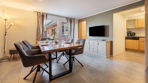 Een moderne eethoek met een tafel, stoelen, een televisie en een keuken op de achtergrond.
