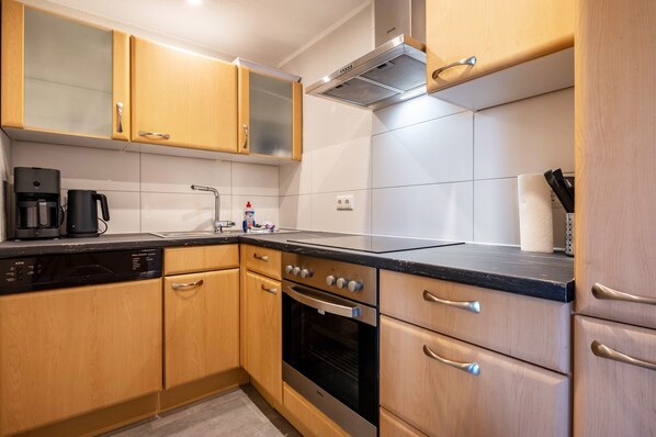 Eine moderne Küche mit Holzschränken, einer schwarzen Arbeitsplatte, Edelstahlgeräten und einem eingebauten Backofen.