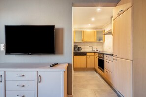 Une cuisine compacte avec un téléviseur fixé au-dessus d’un meuble blanc, des meubles en bois et un lave-vaisselle.